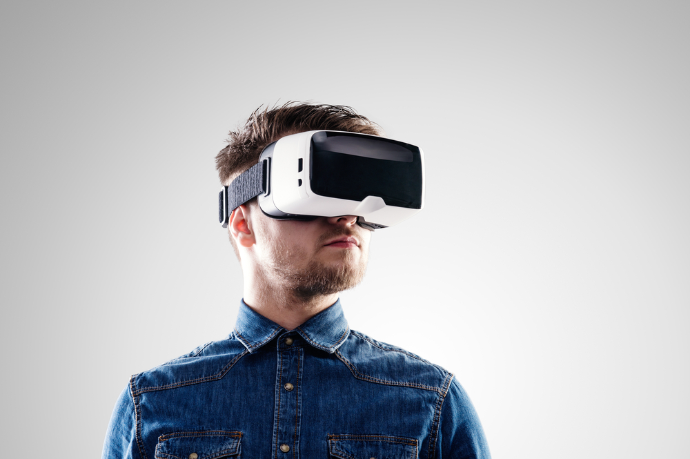 Man wearing virtual reality googles with grey background.